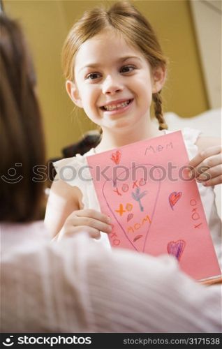 Caucasian girl giving mid adult mother a drawing.