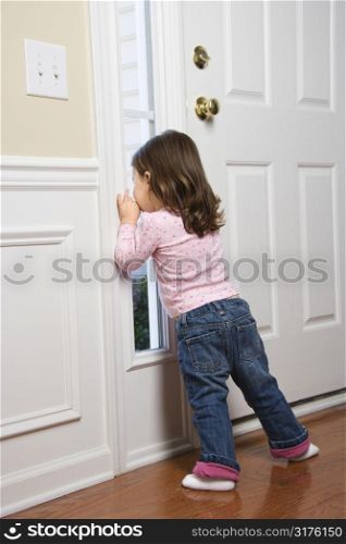 Caucasian girl toddler peeking out of window by door.