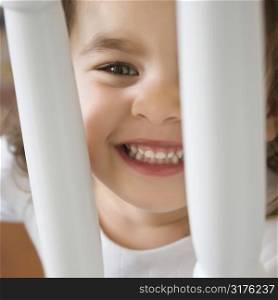 Caucasian girl toddler smiling and peering between railing.