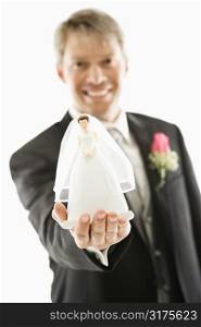 Caucasian groom holding out bride figurine in palm of his hand.