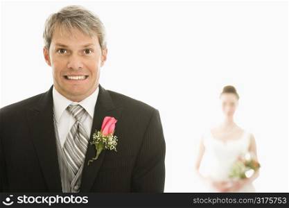 Caucasian groom in foreground with scared expression and Asian bride in background.