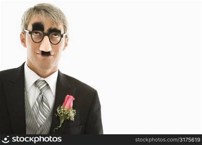 Caucasian groom wearing groucho glasses looking up.