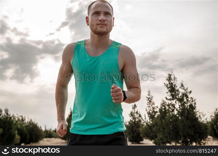 Caucasian guy in a blue t-shirt and black shorts,running over rough terrain. training during sunset