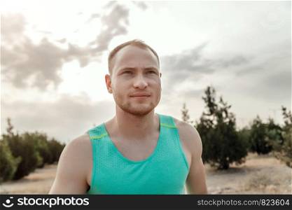 Caucasian guy in a blue t-shirt and black shorts,running over rough terrain. training during sunset