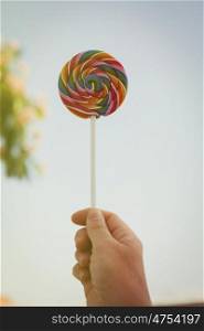 Caucasian hand holding a round lollipop with many colors in a spiral