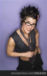 Caucasian Hispanic woman wearing eyeglasses smiling looking at viewer holding necktie standing against purple background.
