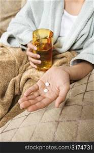 Caucasian/Hispanic young woman holding pills in hand with glass of water.