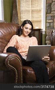 Caucasian/Hispanic young woman sitting in leather chair looking at laptop computer.