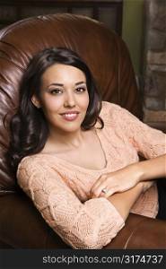Caucasian/Hispanic young woman sitting in leather chair smiling with arms crossed looking at viewer.
