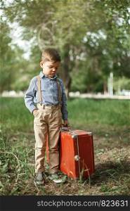 Caucasian little boy in vintage clothes in the Park with an old suitcase and a retro camera in his hands