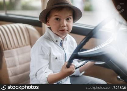 Caucasian little boy in vintage clothes sitting inside a retro car