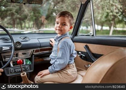 Caucasian little boy in vintage clothes sitting inside a retro car