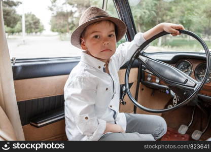 Caucasian little boy in vintage clothes sitting inside a retro car