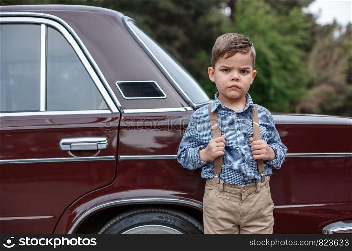 Caucasian little boy in vintage clothes standing next to a retro car