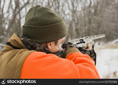 Caucasian male aiming shotgun out towards woods.