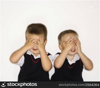 Caucasian male children twins with hands over eyes.