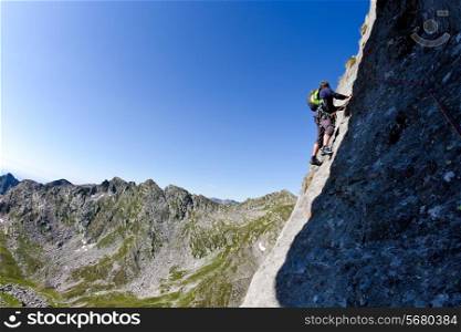 Caucasian male climber climbing a steep wall. In background a summer alpine landscape. Clear sky, day light. West italian Alps, Europe.