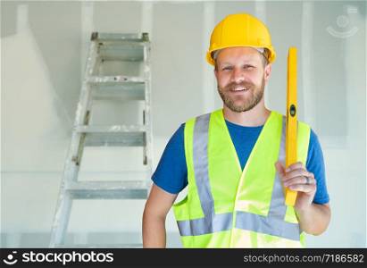 Caucasian Male Contractor With Hard Hat, Level and Safety Vest At Construction Site.