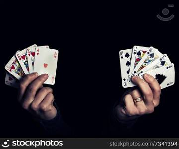 Caucasian male hands holding two royal flush poker combination of heart and spade. Low-key lighting composition, isolated over the black background