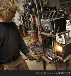 Caucasian male metalsmith heating metal in forge.