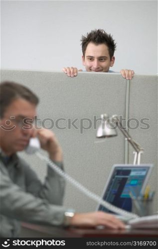 Caucasian Male Office Worker Peeking Over The Cubicle Wall At His Coworker