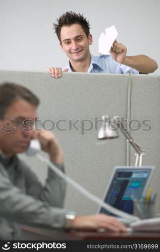Caucasian Male Office Worker Throwing A Paper Airplane At His Cubicle Neighbor