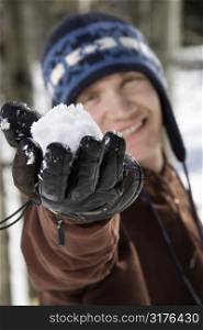 Caucasian male teenager holding snowball out towards viewer.