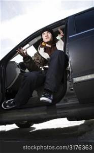 Caucasian male teenager sitting in car making hand gesture.