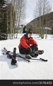 Caucasian male teenager sitting on snow with ski gear.