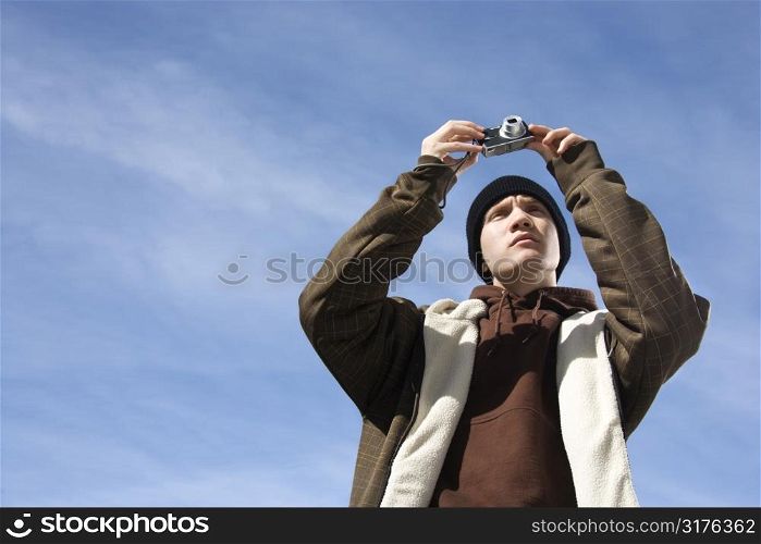 Caucasian male teenager taking a picture with a digital camera.