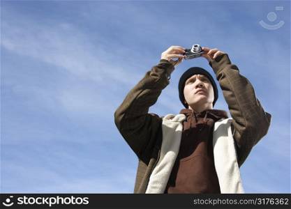 Caucasian male teenager taking a picture with a digital camera.