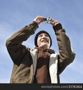 Caucasian male teenager taking a picture with a digital camera.