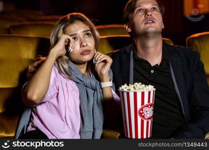 Caucasian man and woman watching a sad movie and his girlfriend crying