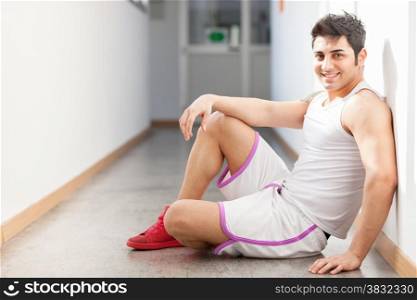 Caucasian man in sportswear is sitting on the floor in corridor