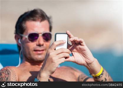 Caucasian man is checking his phone while relaxed on the beach
