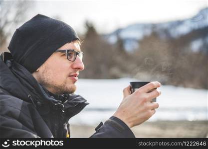 Caucasian man is holding a cup of tea outdoors, winter time