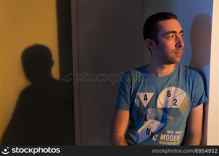 Caucasian man leaning against the wall and looking away when he is in deep thought. He is in a room during sunset at the afternoon.