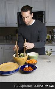 Caucasian man making salad on kitchen counter.