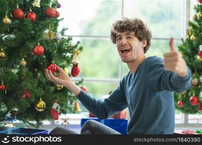 Caucasian man show thumbs up to camera during decorate the Christmas tree with happiness to stay at home and celebrating.