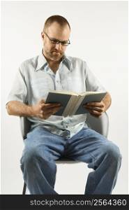 Caucasian man sitting in chair reading book against white background.