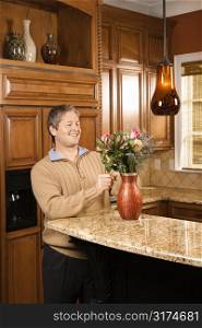 Caucasian man smiling and arranging flowers in vase in kitchen.