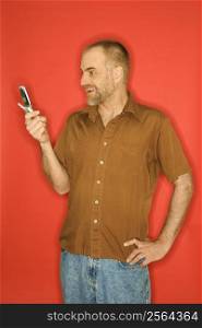 Caucasian man smiling and looking at cellphone standing against orange background.