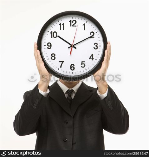Caucasian man wearing suit holding clock in front of face.