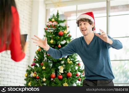 Caucasian man with Christmas hat show action of online greeting with other people that support by his girlfriend at home during Christmas festival.