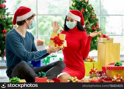Caucasian man with hygiene mask show the present or gift to his couple woman and she action of surprise for Christmas celebration during pandemic of Covid-19.