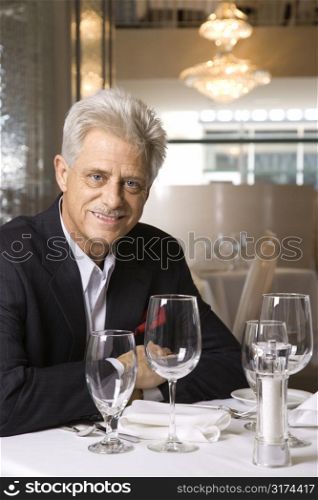 Caucasian mature adult male sitting at restaurant table looking at viewer smiling.