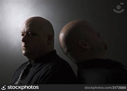 Caucasian mid adult bald identical twin men standing back to back.