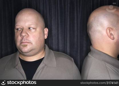 Caucasian mid adult bald man looking away from his identical twin.