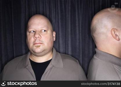 Caucasian mid adult bald man looking to side at his identical twin.