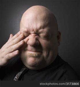 Caucasian mid adult bald man rubbing eye and making facial expression.